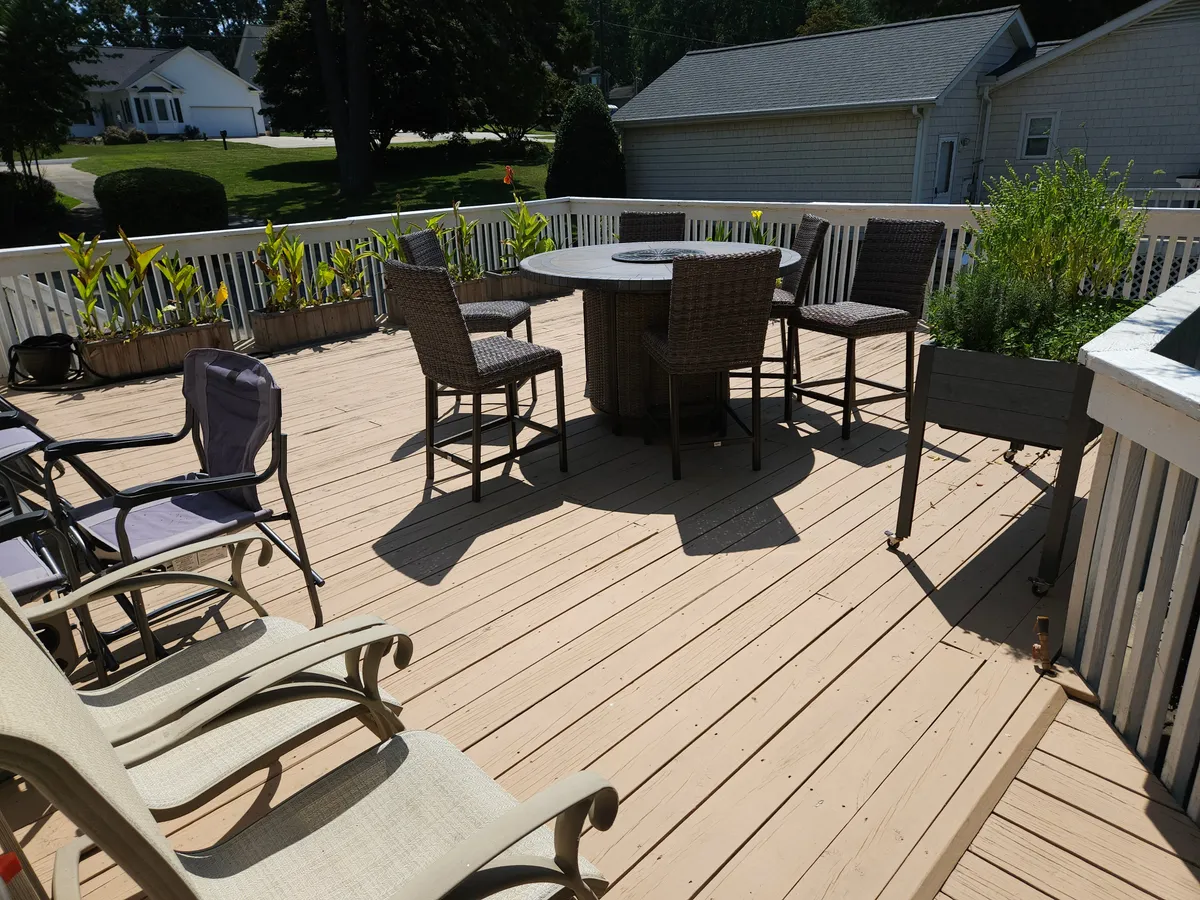 An exterior shot featuring a round dining table with high chairs, surrounded by planter boxes and lounge chairs. The setting is ideal for dining or socializing outdoors, with views that likely overlook the scenic lake.