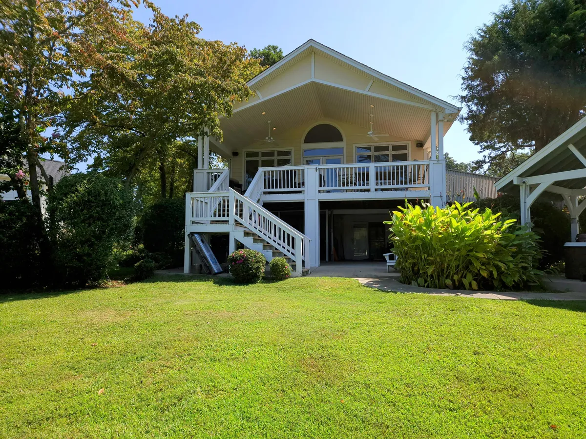 A spacious outdoor deck surrounded by lush greenery, with stairs leading up to the deck and comfortable seating areas arranged for social interaction. The scene is inviting and suggests a space designed for family gatherings, barbecues, and unwinding as the sun sets.