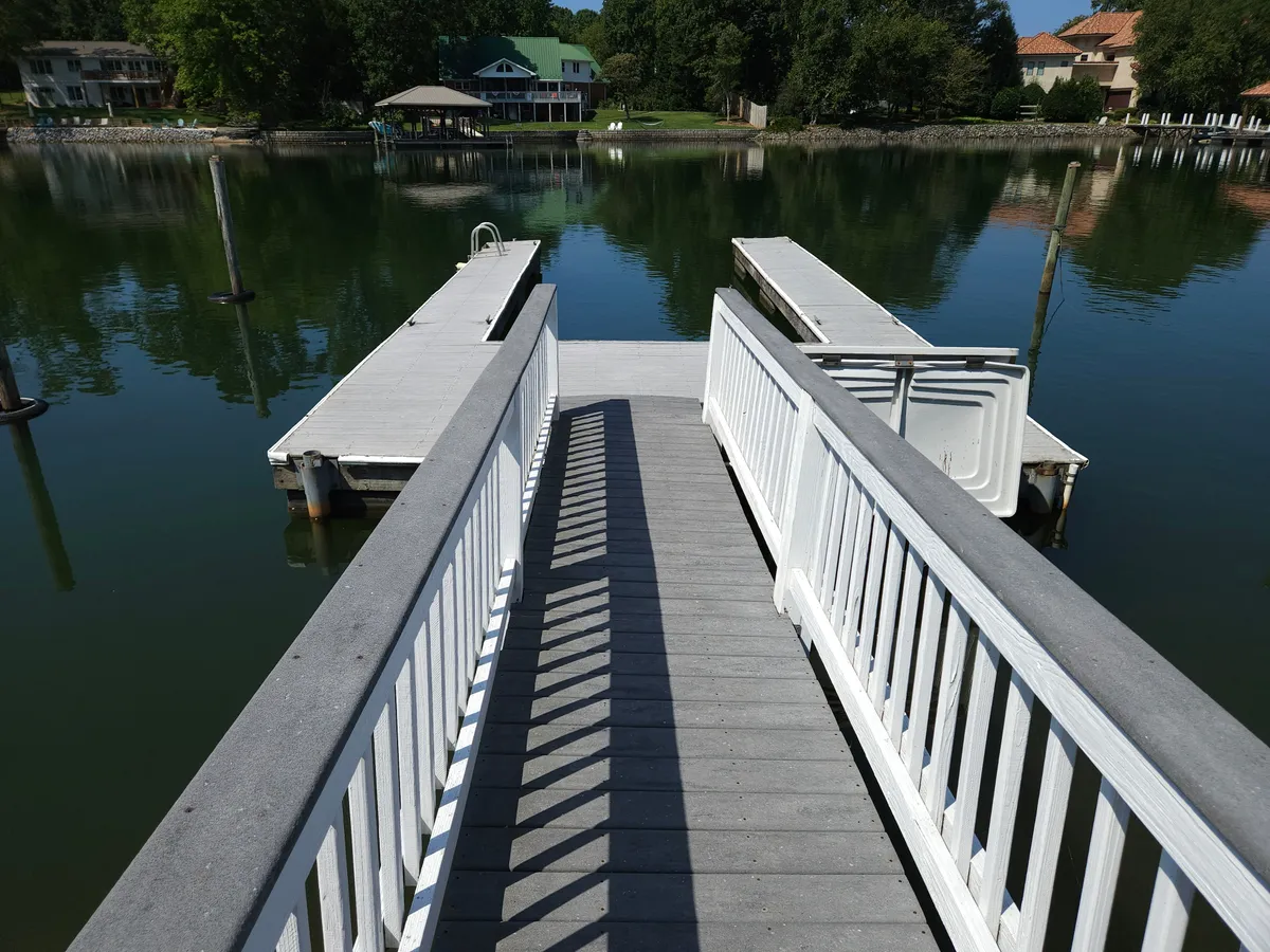 A wooden dock extends over calm lake waters, surrounded by lush greenery. The scene exudes tranquility and invites activities like boating, fishing, or simply taking in sunset views. There are no other people in the image, enhancing the sense of privacy.
